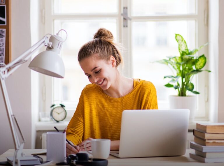 Sixth-form student smiling while studying at a desk with a laptop