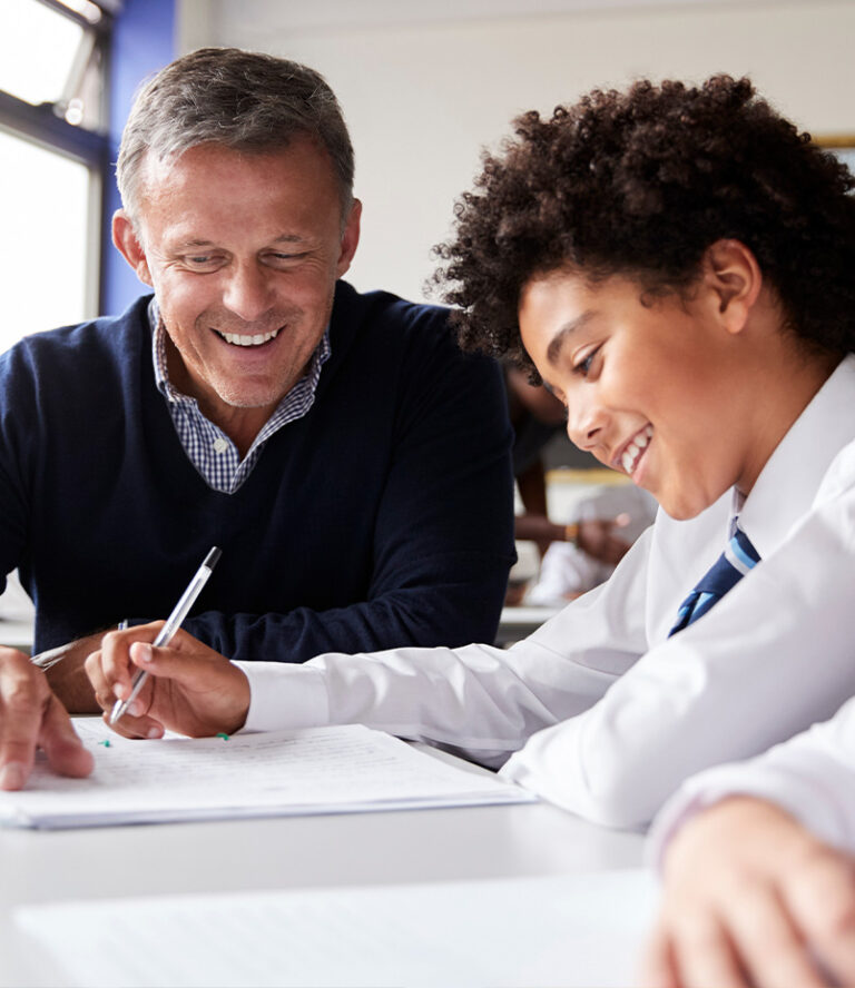 Tutor helping a secondary student with written work at a desk