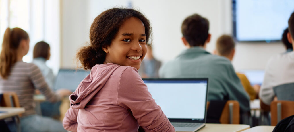 Secondary student smiling while working on a laptop in class